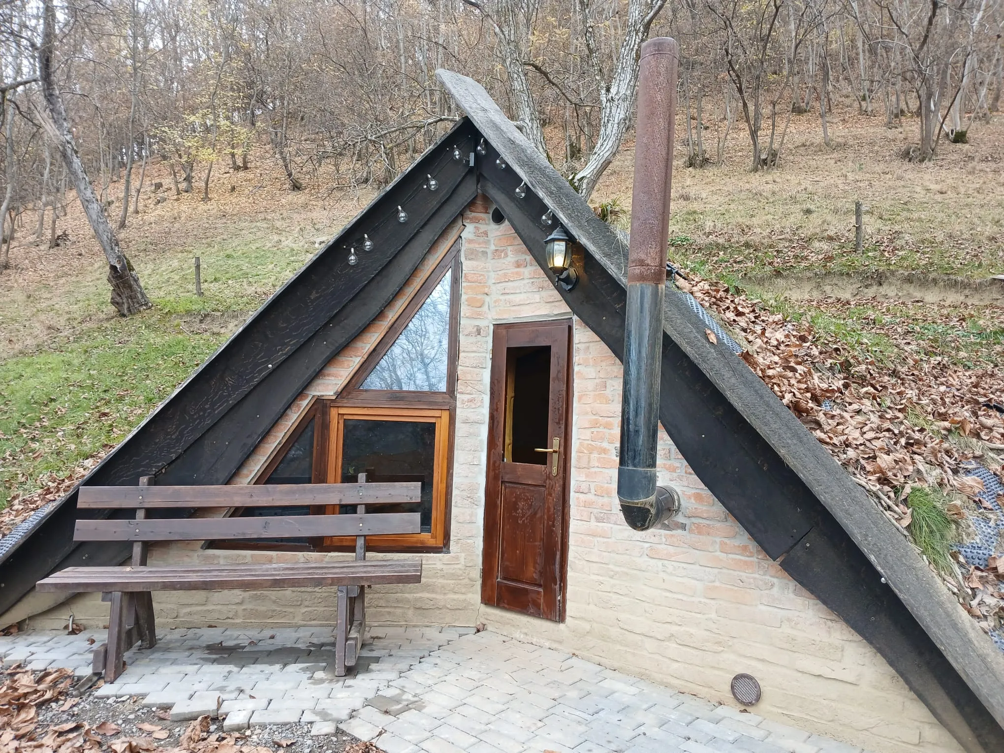 A-frame brick cabin with a chimney among the bare trees